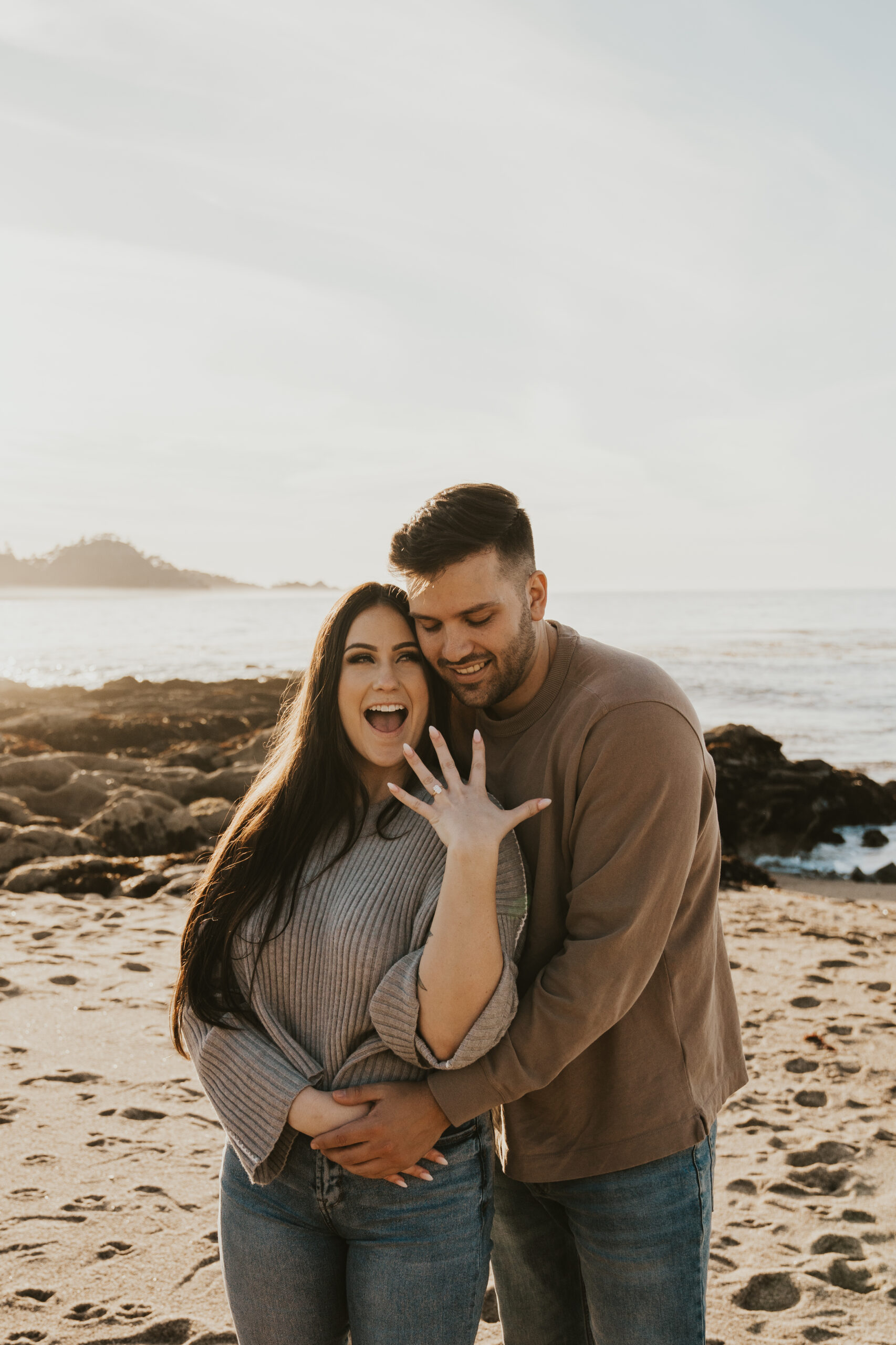 Newly engaged couple shows off the ring standing on the beach in Carmel-by-the-Sea