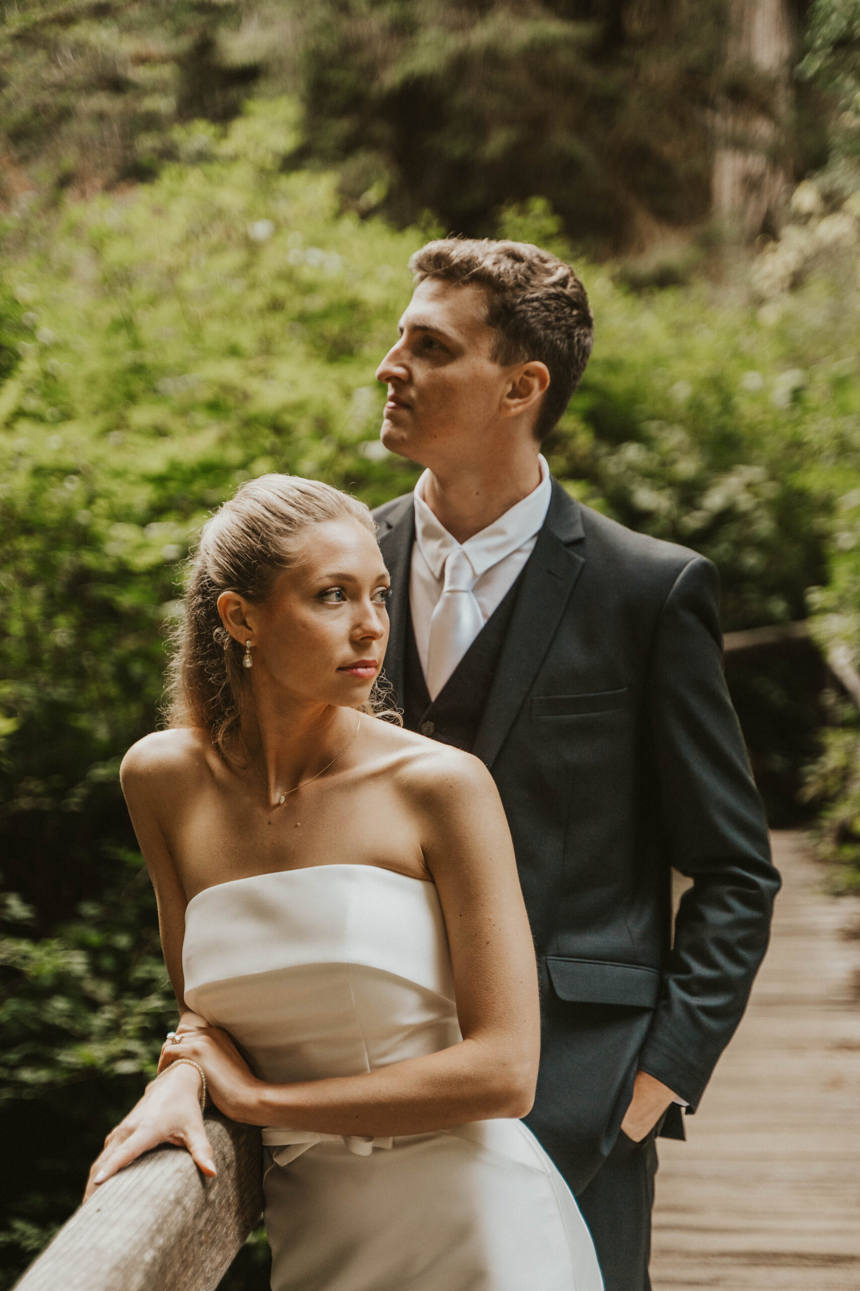 Elopement Couple stand in wedding dress and suit on bridge surrounded by foliage